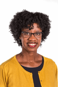 A woman with curly black hair and glasses smiling, wearing a yellow cardigan.