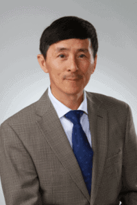 A man in a gray checkered suit and blue tie posing for a professional portrait.