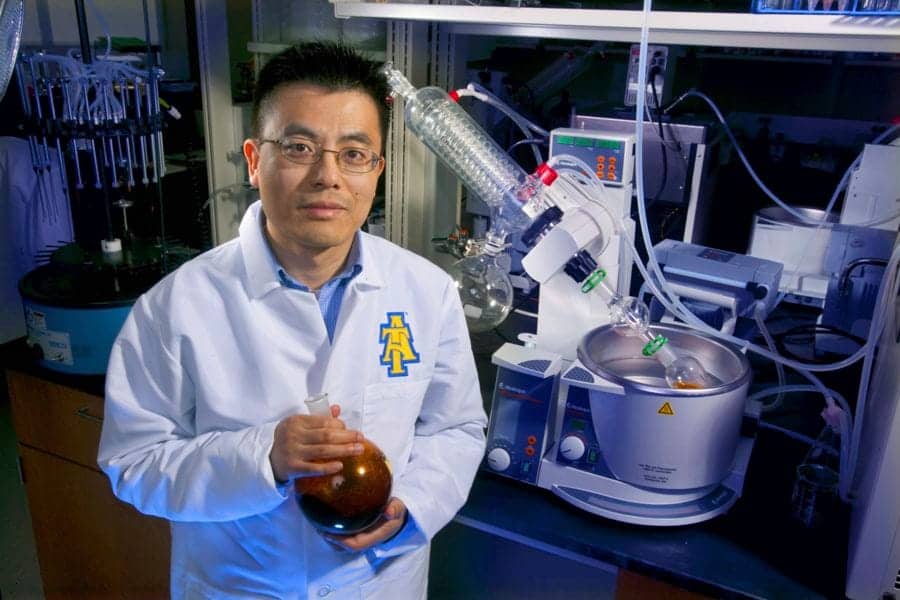 A scientist in a laboratory holding a flask with a brown liquid, surrounded by scientific equipment.