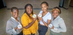 Empowered young women holding CAES News badges at an indoor event.