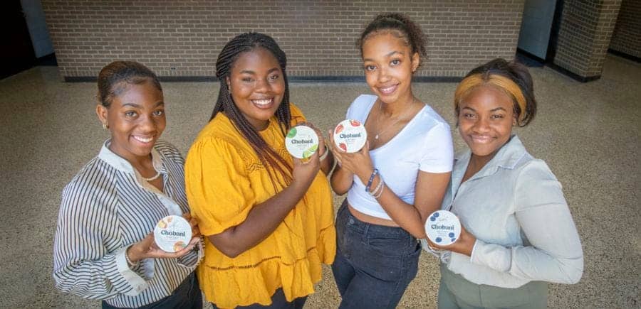 Empowered young women holding CAES News badges at an indoor event.
