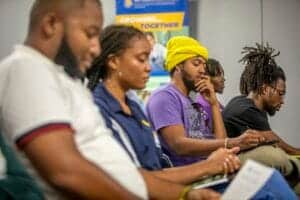 Young adults attending a community event, engaging with digital devices and reading materials, promo.