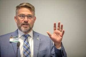 Kevin Leonard speaking at a conference, wearing a suit and glasses, gesturing with his hand during a.