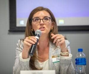 Accessible, professional woman speaking into microphone at conference, wearing glasses and business.