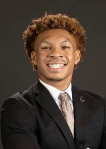 A young professional man smiling in a black suit and tie, portrait for business or corporate profile.