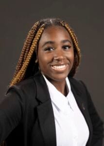 A woman with braided hair smiling in professional attire for CAES News.