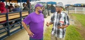 A woman and a man having a conversation at an outdoor event, with a tractor and people in the backgr.