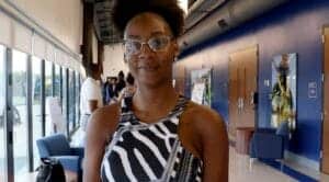 A woman with glasses and natural hair at an indoor event or conference.