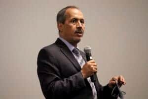 Empowered male speaker in formal suit delivering a presentation with a microphone at a conference.