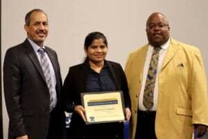 Award recipient holding certificate with two men in formal attire at a professional event.