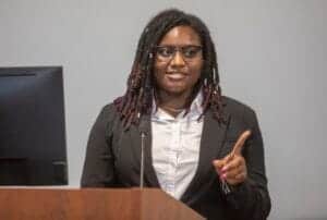 A woman with dreadlocks and glasses speaking at a conference or seminar.