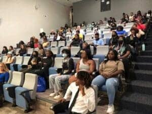 Students attending a lecture or seminar in a modern classroom setting, wearing masks and paying atte.