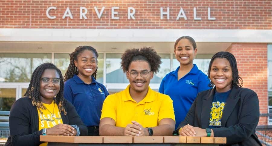 High school students smiling outside Carver Hall, promoting education and student success.