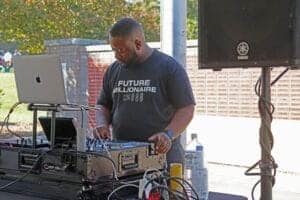 DJ performing at outdoor event with sound equipment and laptop, showcasing modern music technology.