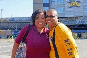 A woman and a man smiling outside a stadium with CAES News branding.