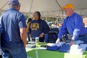 CAES News booth at an outdoor event with smiling staff engaging visitors.