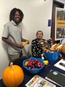 Bright young man and woman at a community event with pumpkins, apples, and informational materials f.