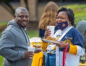 People enjoying food and drinks at an outdoor event, wearing masks and casual clothing.