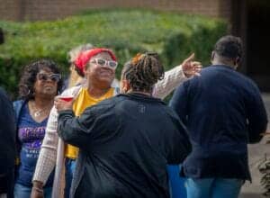 A woman in a yellow shirt and red headscarf speaking passionately to a group outdoors.