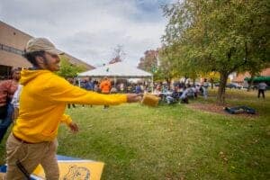 Person tossing a drink at an outdoor community event with tents and trees.