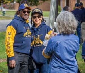 NC A&T Aggies alumni couple smiling at an outdoor event, wearing matching blue and gold hoodies.