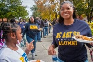 Celebrating A&T State University alumni at outdoor event with smiling students and community members.
