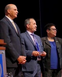 Three professionals at an award ceremony, formal attire, recognition event, business leaders.