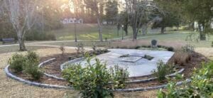 A lush park with a circular stone monument and surrounding greenery during sunset.
