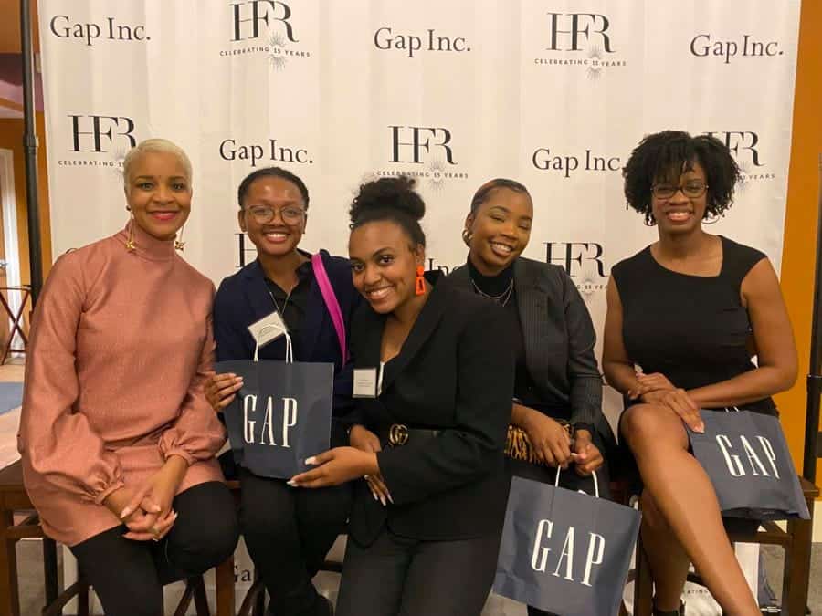 A woman in a pink blouse and four women in black outfits smiling at a GAP event.