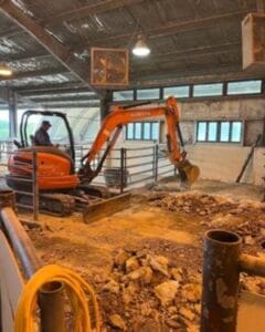 Excavator working on construction site indoors with dirt and debris.