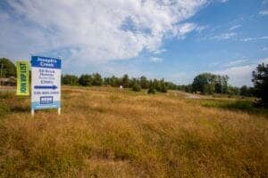 Vacant land for sale with real estate sign in a grassy field under a blue sky.