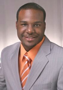 Professional African-American man in gray suit and orange tie smiling for business portrait.