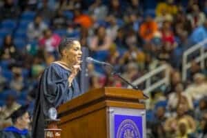 Graduation speaker delivering speech at university ceremony with audience in background.