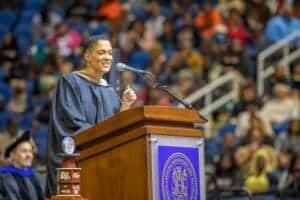 Graduation speaker delivering speech at university ceremony with audience in background.