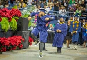 Graduates celebrating at a commencement ceremony with joyful dancing and colorful academic regalia.