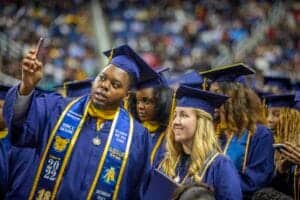 Graduates in blue caps and gowns celebrating at a graduation ceremony.