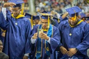 Graduates in blue caps and gowns celebrating at a graduation ceremony.