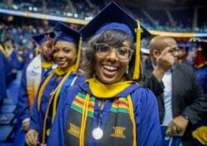 Graduates celebrating at a graduation ceremony in caps and gowns with colorful stoles.