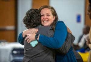 A woman happily hugging another person in a professional setting.