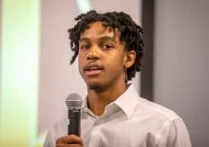 Young man speaking into a microphone at a conference or event.