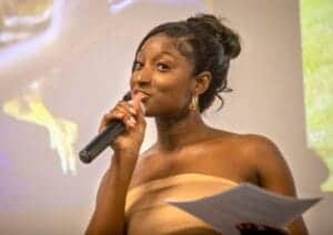 Woman speaking into microphone at event, holding paper, in a professional setting.