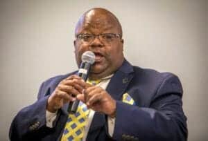 African American man speaking into microphone at conference or event.