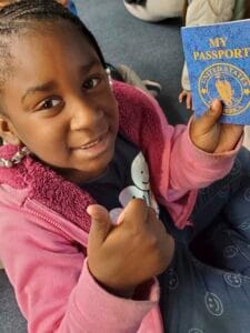 A girl holding a blue U.S. passport and giving a thumbs-up gesture.