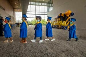 Graduates in blue caps and gowns walking in a line at a graduation ceremony.