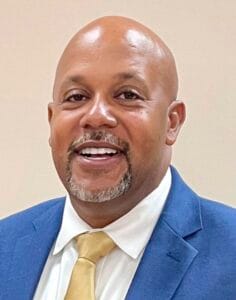 A man in a blue suit and yellow tie smiling at the camera.