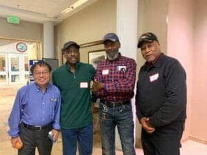 Diverse group of four men smiling and posing together at a community event, showcasing collaboration.