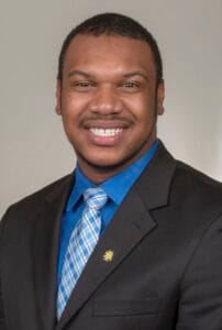 A smiling man in a business suit with a blue shirt and patterned tie, professional portrait.