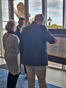 Agricultural professionals discussing research at conference with display board and scenic outdoor v.