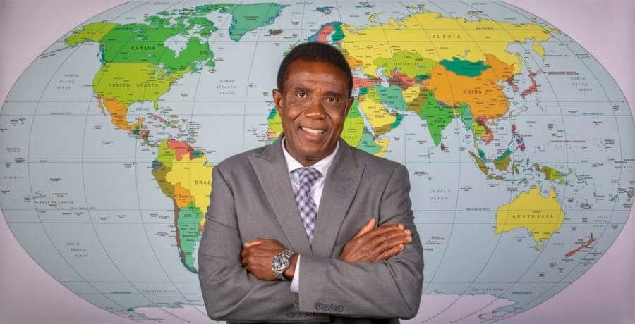 Global businessman standing in front of a world map, representing international news and global conn.