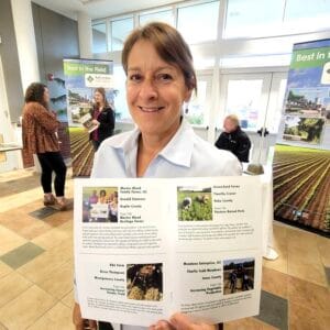 Woman holding CAES News poster at event.